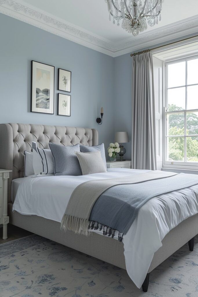 Small bedroom featuring blue-gray walls, crisp white bedding, mirrored furniture, and soft lighting.